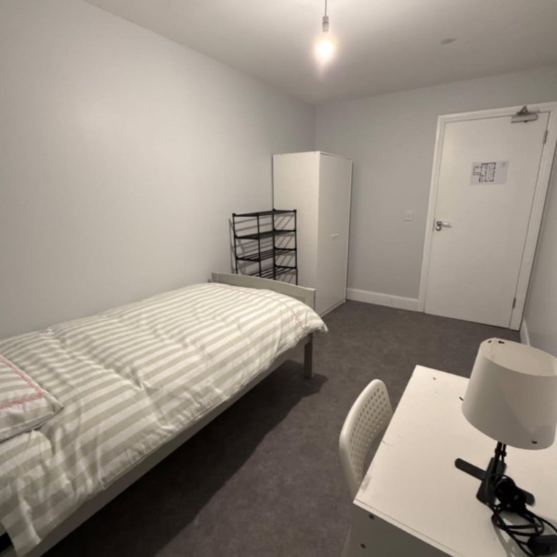 Small bedroom interior with bed, desk, wardrobe, and shoe rack. Neutral decor.