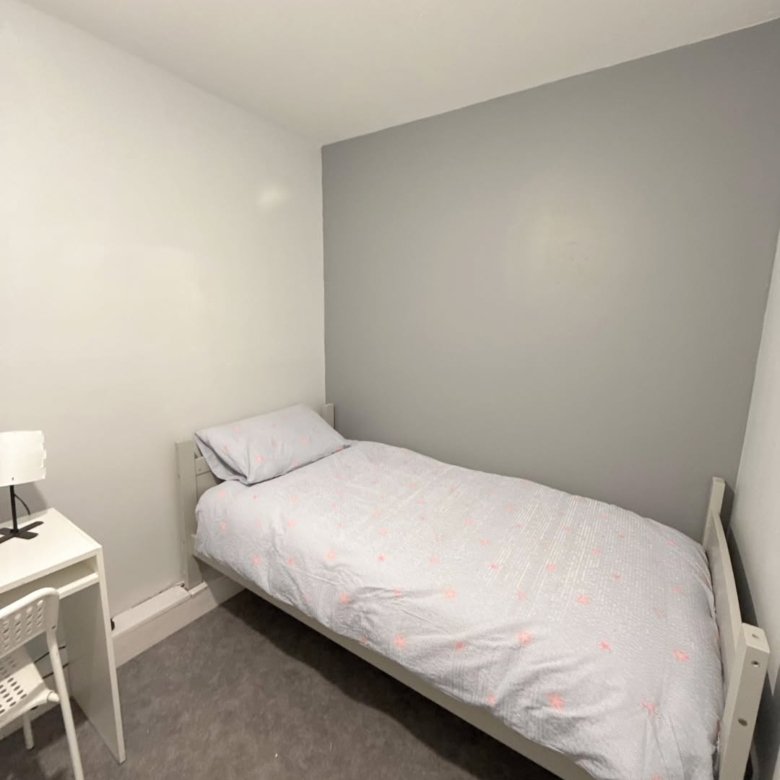 Small bedroom with single bed, desk, and gray/white walls. Minimalist interior design.