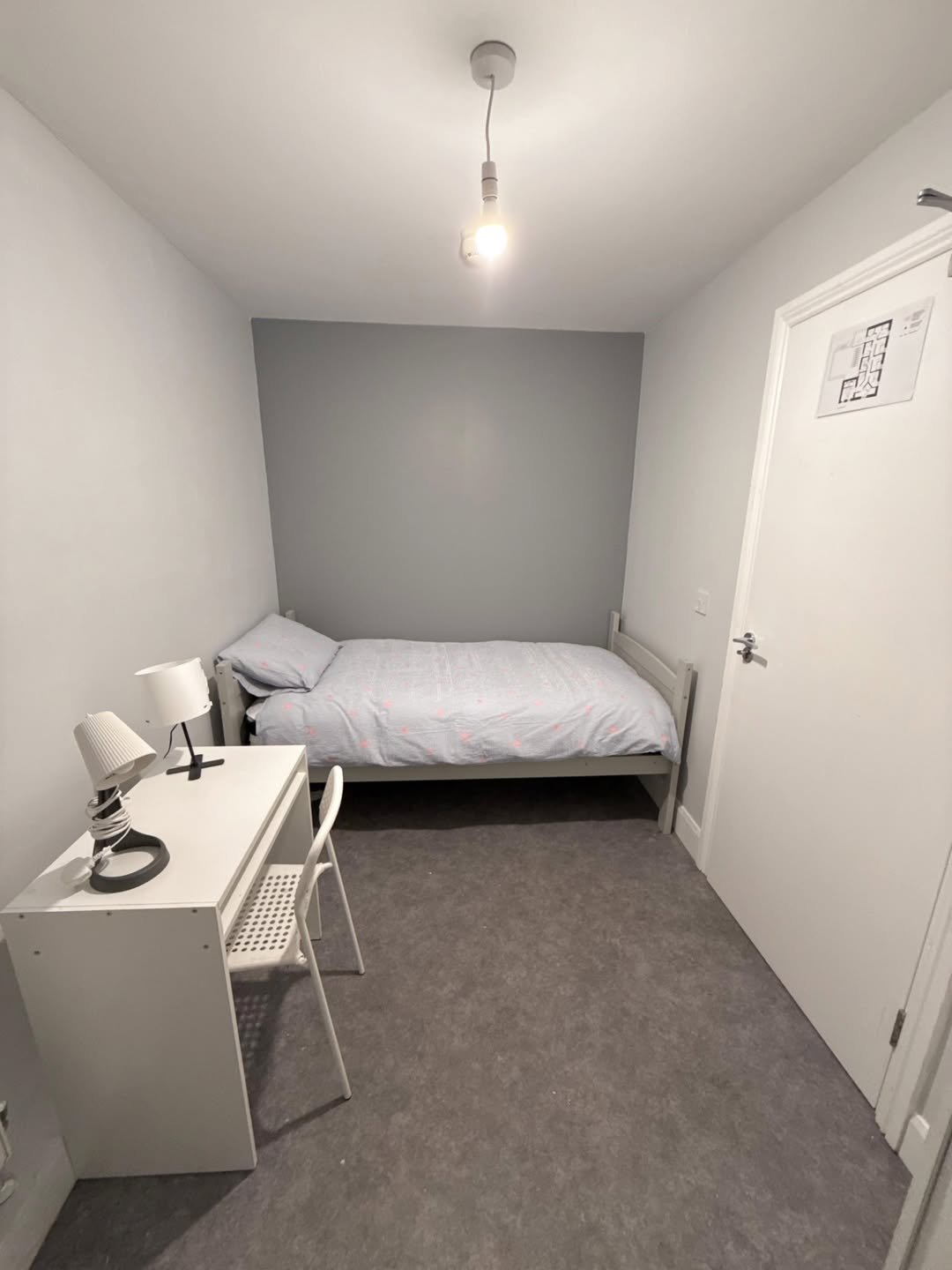 Small bedroom with single bed, desk, and minimal decor in a compact space.