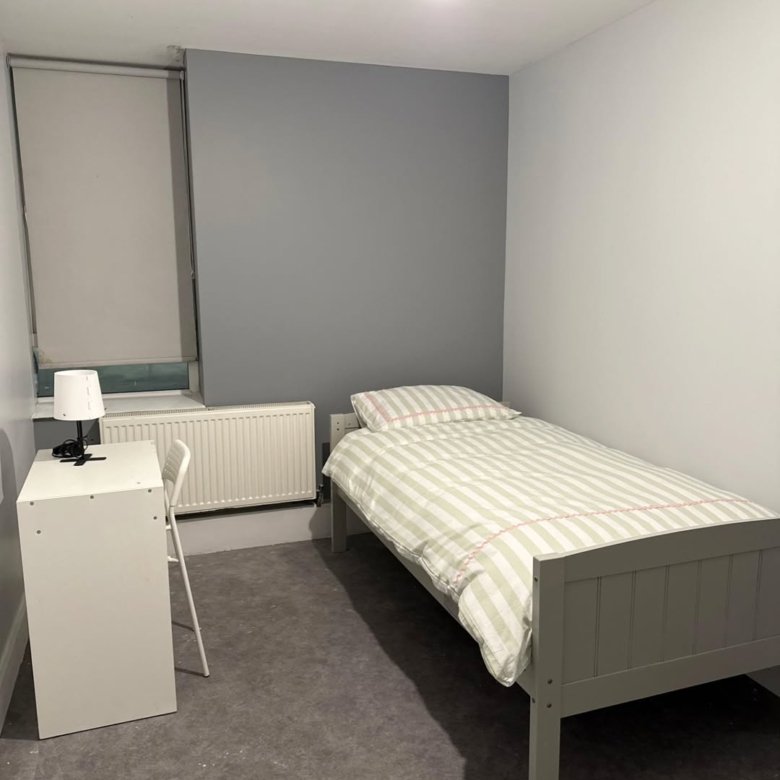 Small bedroom with single bed, desk, radiator, and grey accent wall. Minimalist interior design.