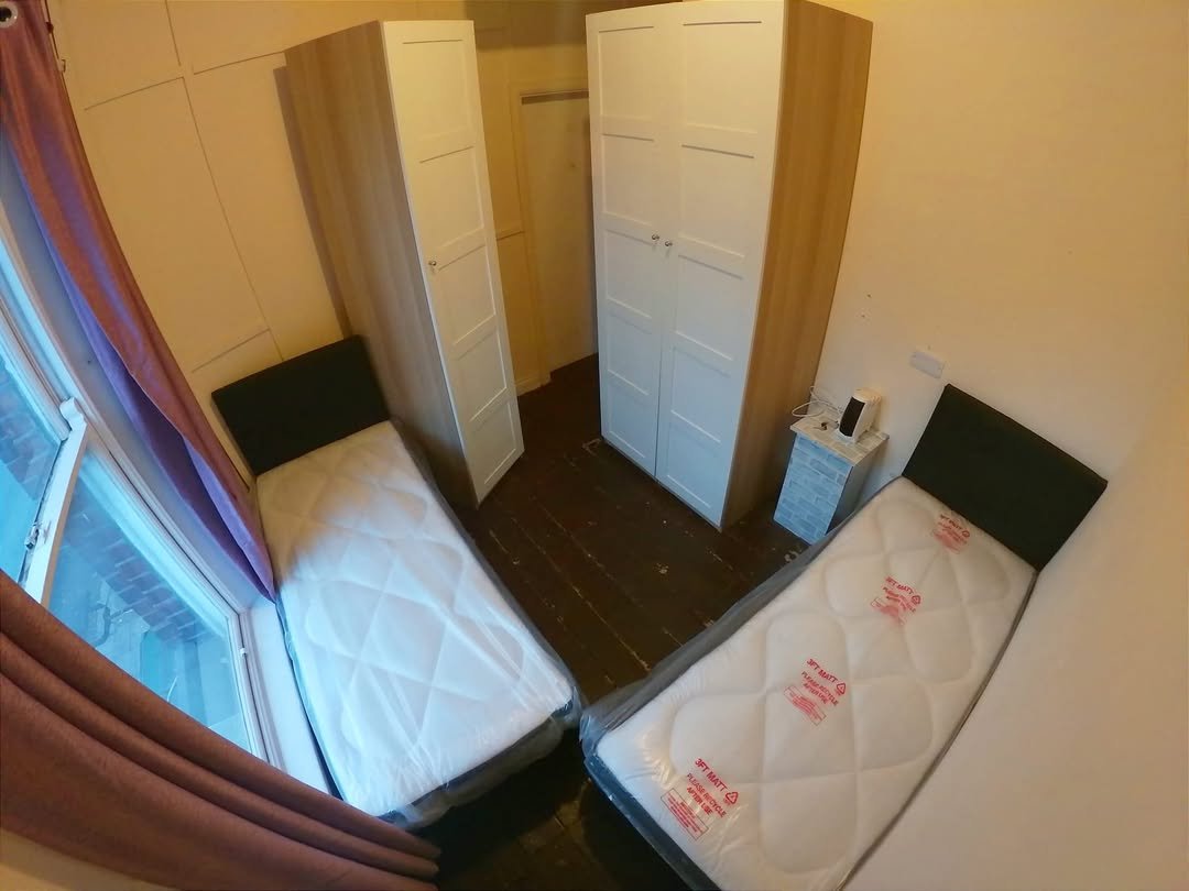 Small Bedroom Twin Beds Wardrobes Small bedroom with two twin beds, wardrobes, and window with purple curtains.