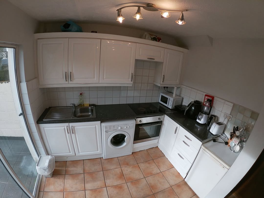 Small kitchen with white cabinets, washing machine, and terracotta floor tiles.