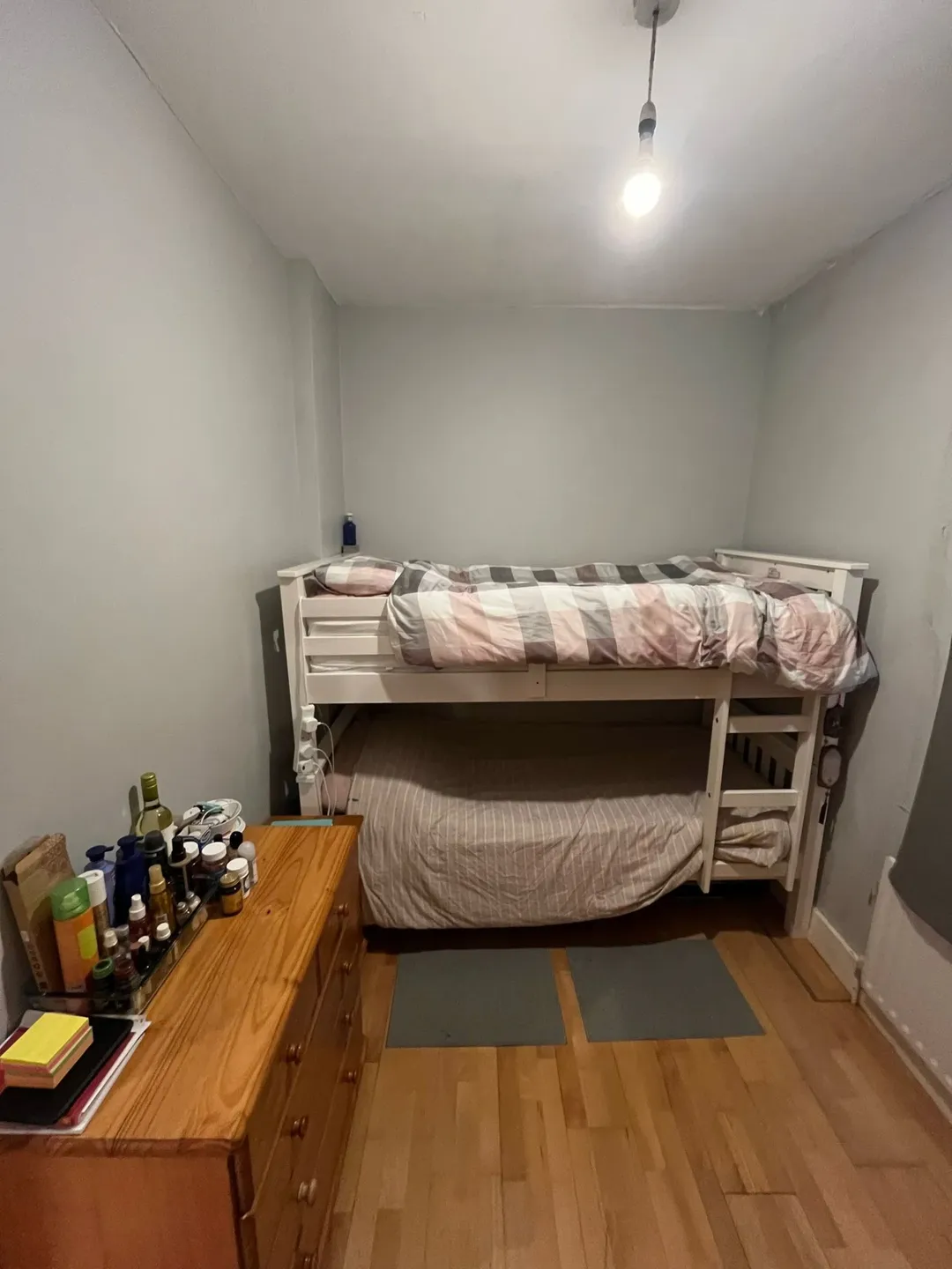 Small room with white bunk bed, wooden dresser, and hardwood floor.