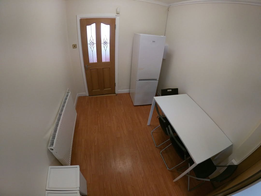 Small room with fridge, table, chairs, and radiator. Neutral tones.