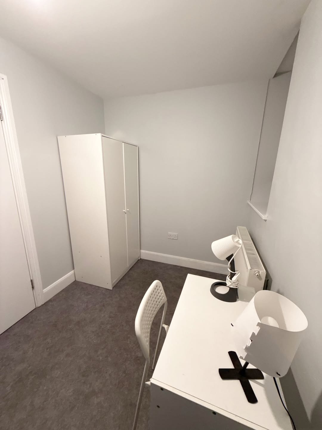 Small room with white wardrobe, desk, chair, and two lamps.