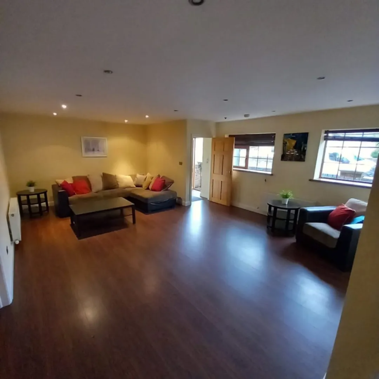 Spacious living room with brown sectional sofa, wood floors, and natural light from windows.