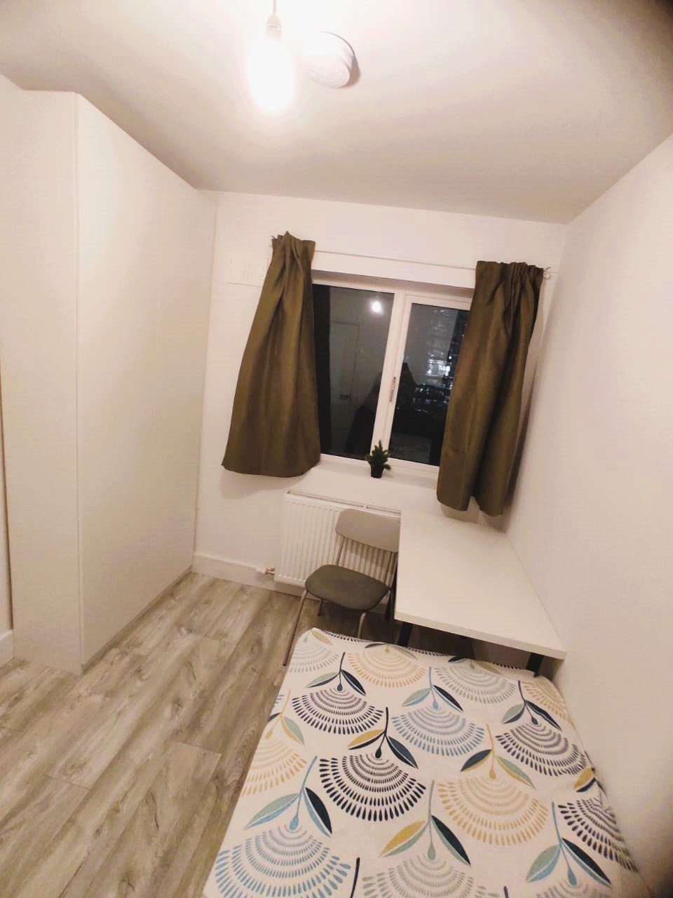 Cozy bedroom with bed, desk, chair, and wardrobe, featuring a window with brown curtains. – Ghar.ie property listing