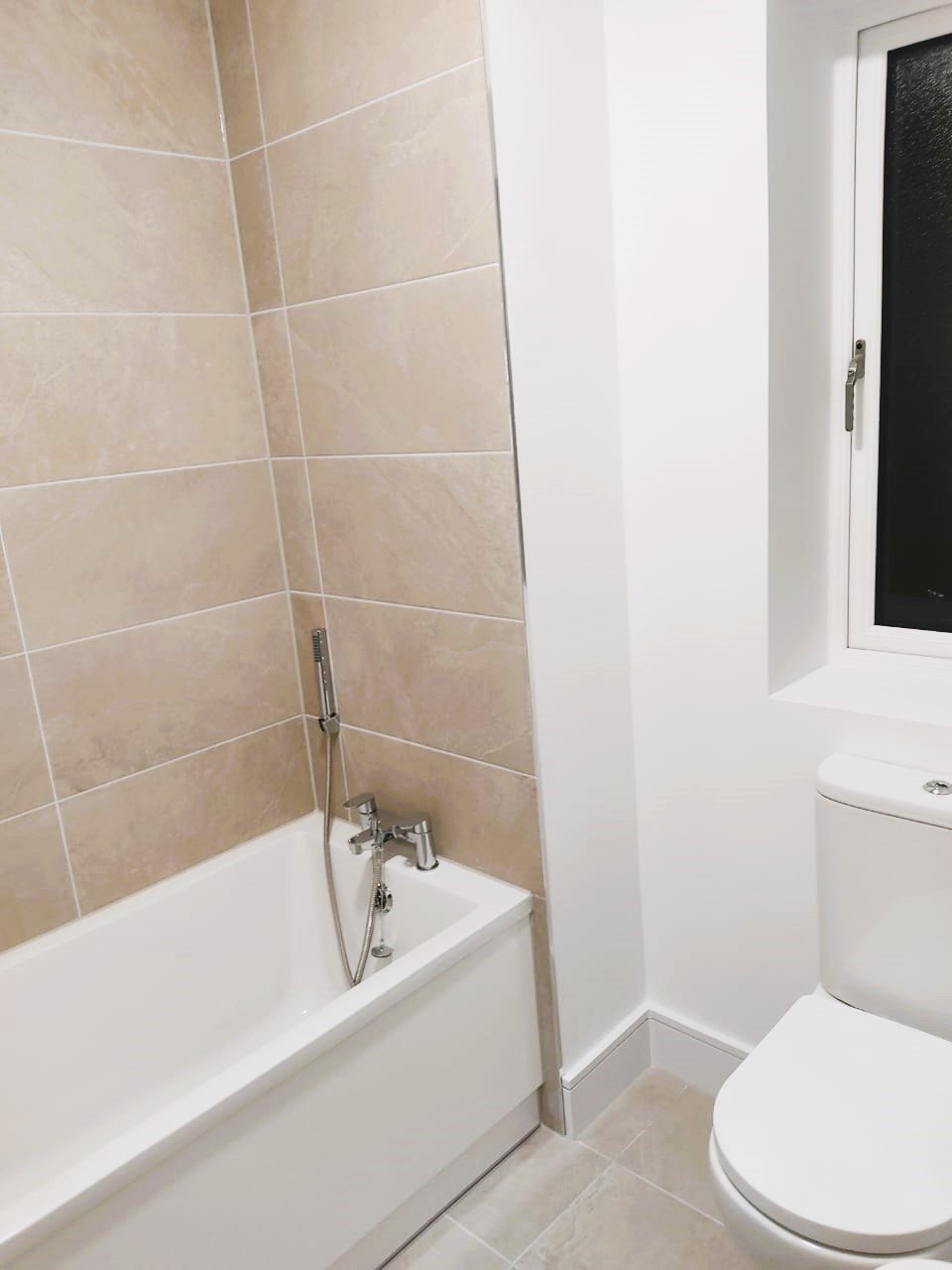 Modern bathroom with beige tiled shower walls, white bathtub, and toilet. – Ghar.ie property listing