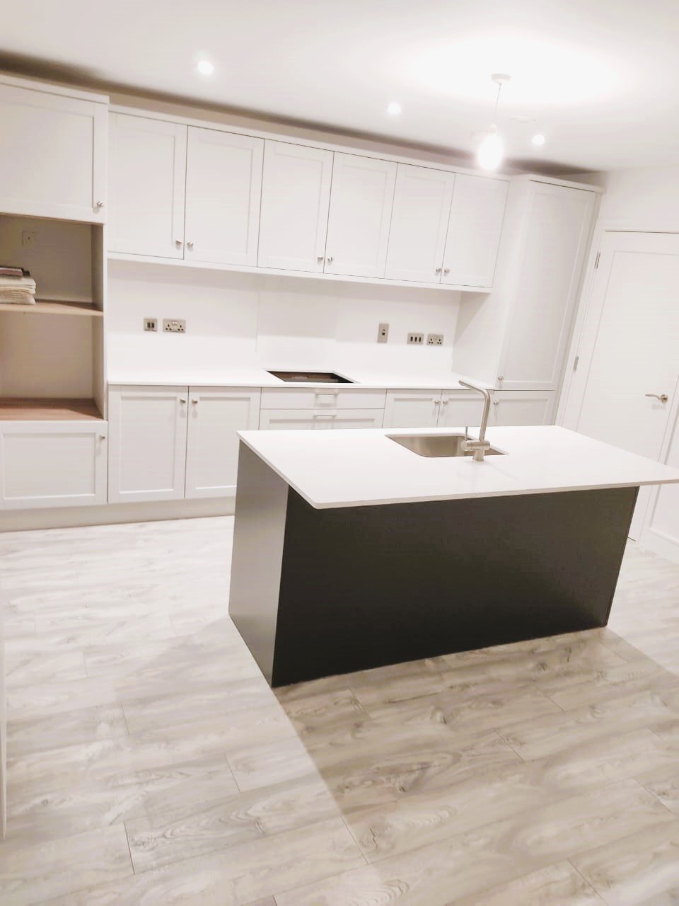 Modern white kitchen with a dark gray island and light wood floors. – Ghar.ie property listing