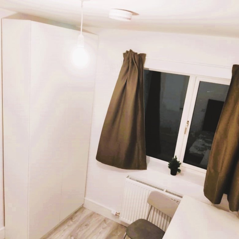 White wardrobe and chair next to a window with brown curtains in a room. – Ghar.ie property listing