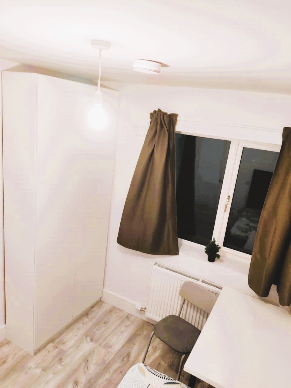White wardrobe and chair next to a window with brown curtains in a room. – Ghar.ie property listing